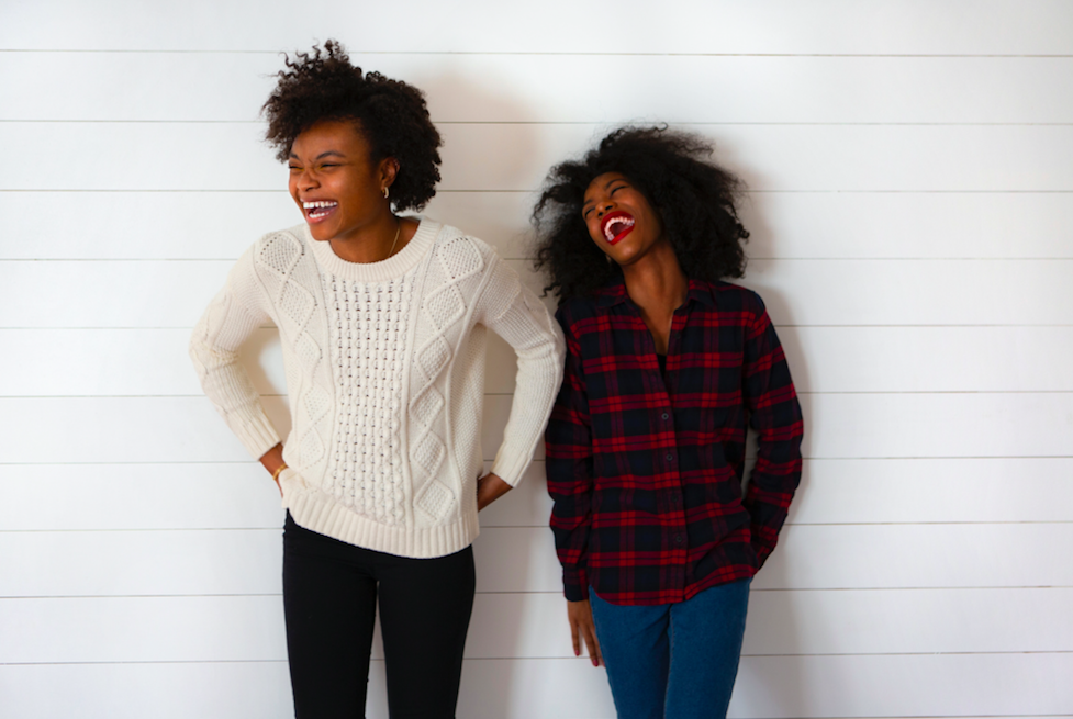 two people standing against white wall laughing