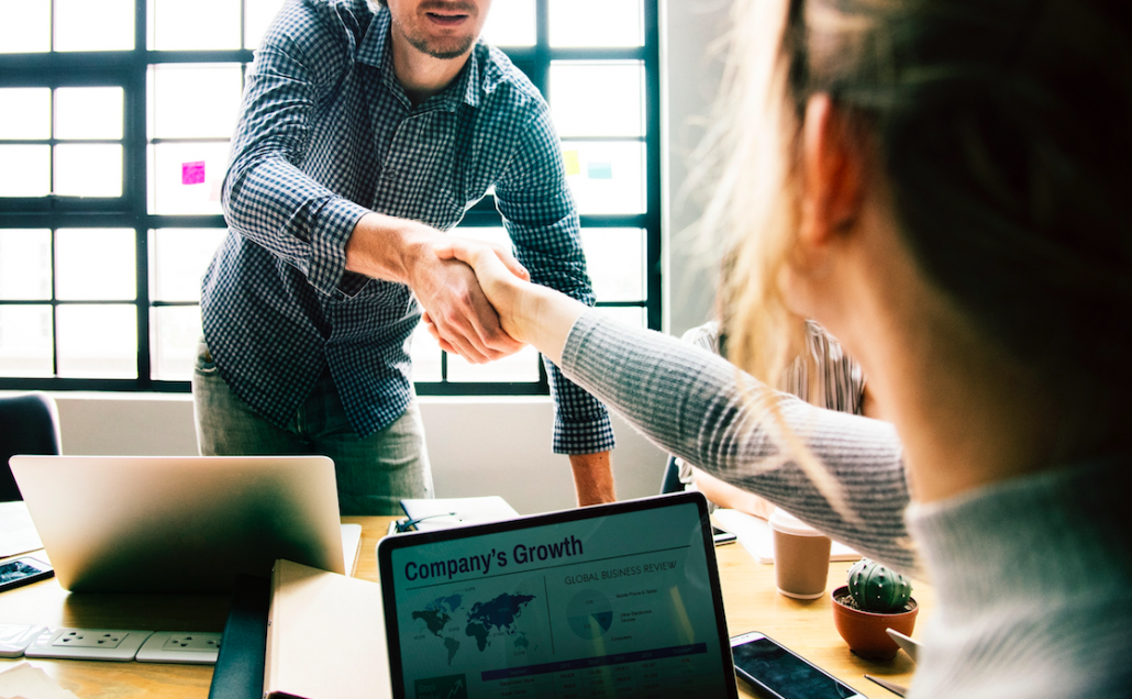 shaking hands over table with computer