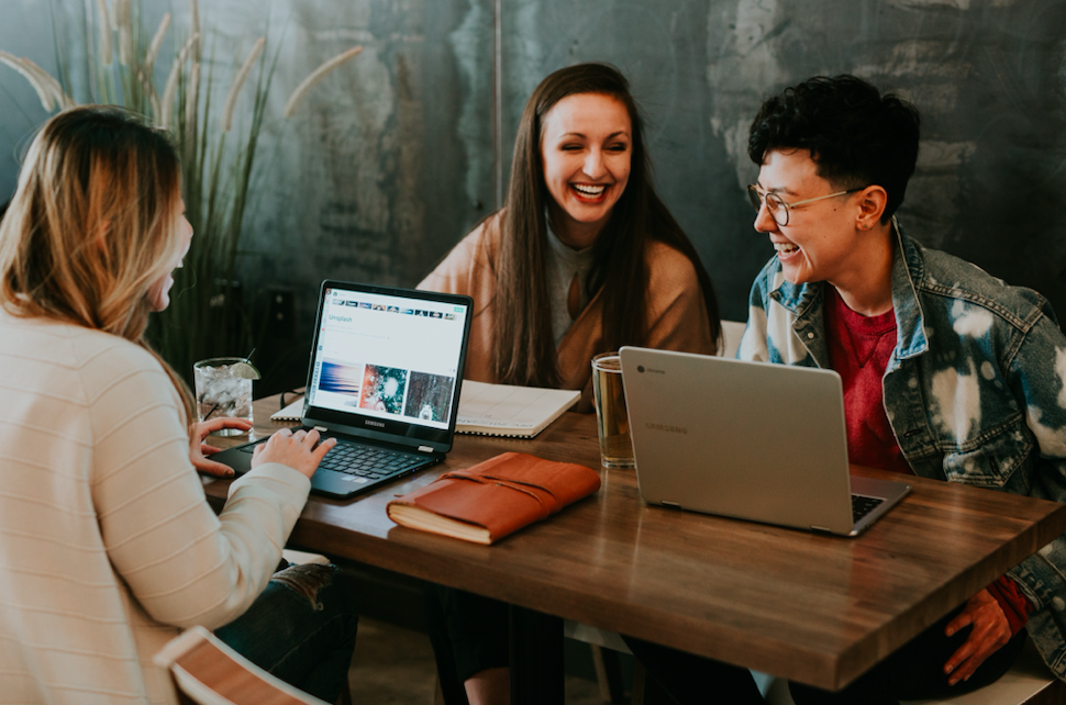 three people at table talking over computers